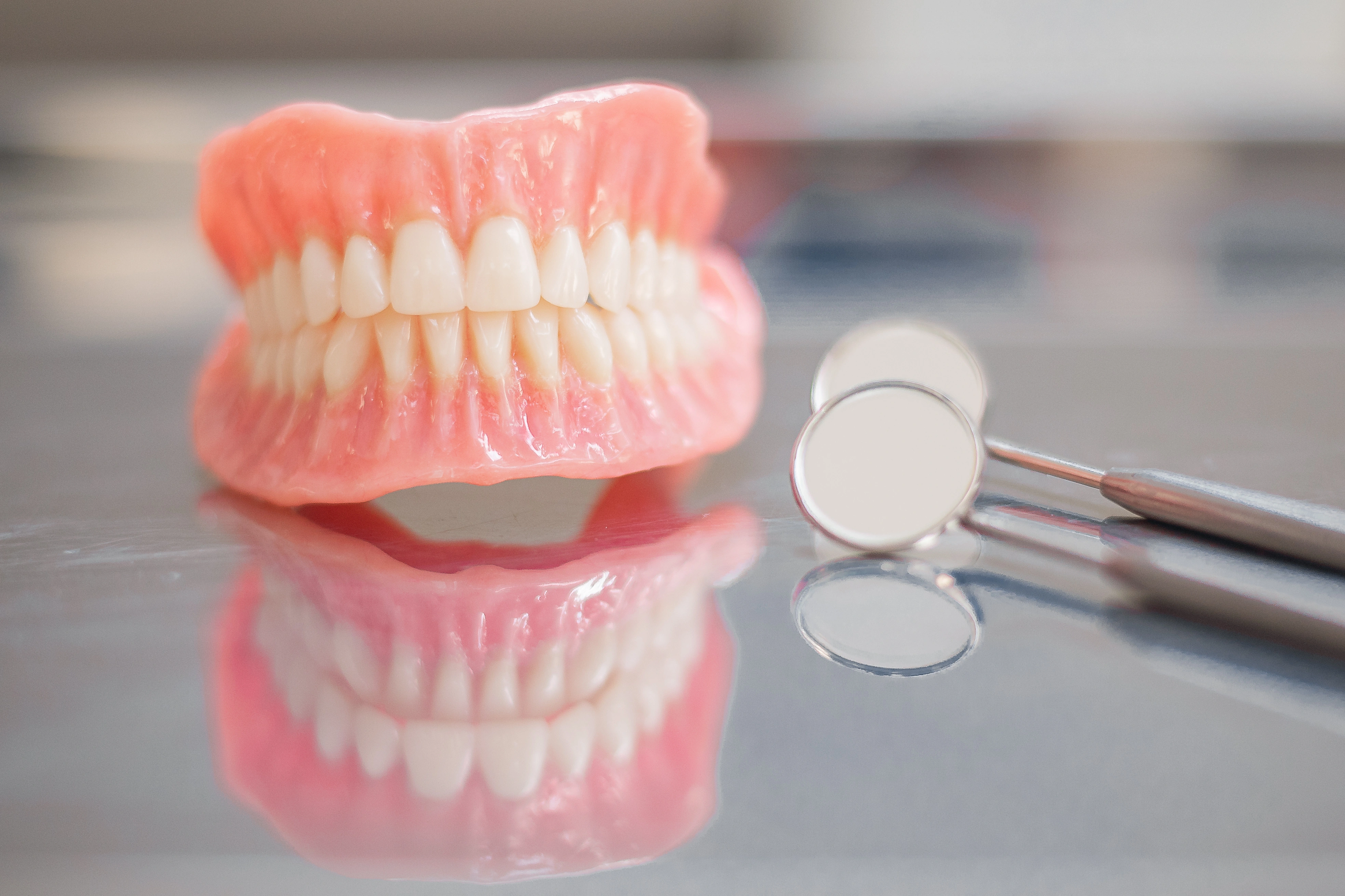 A set of full dentures on a metal surface with dental mirrors.