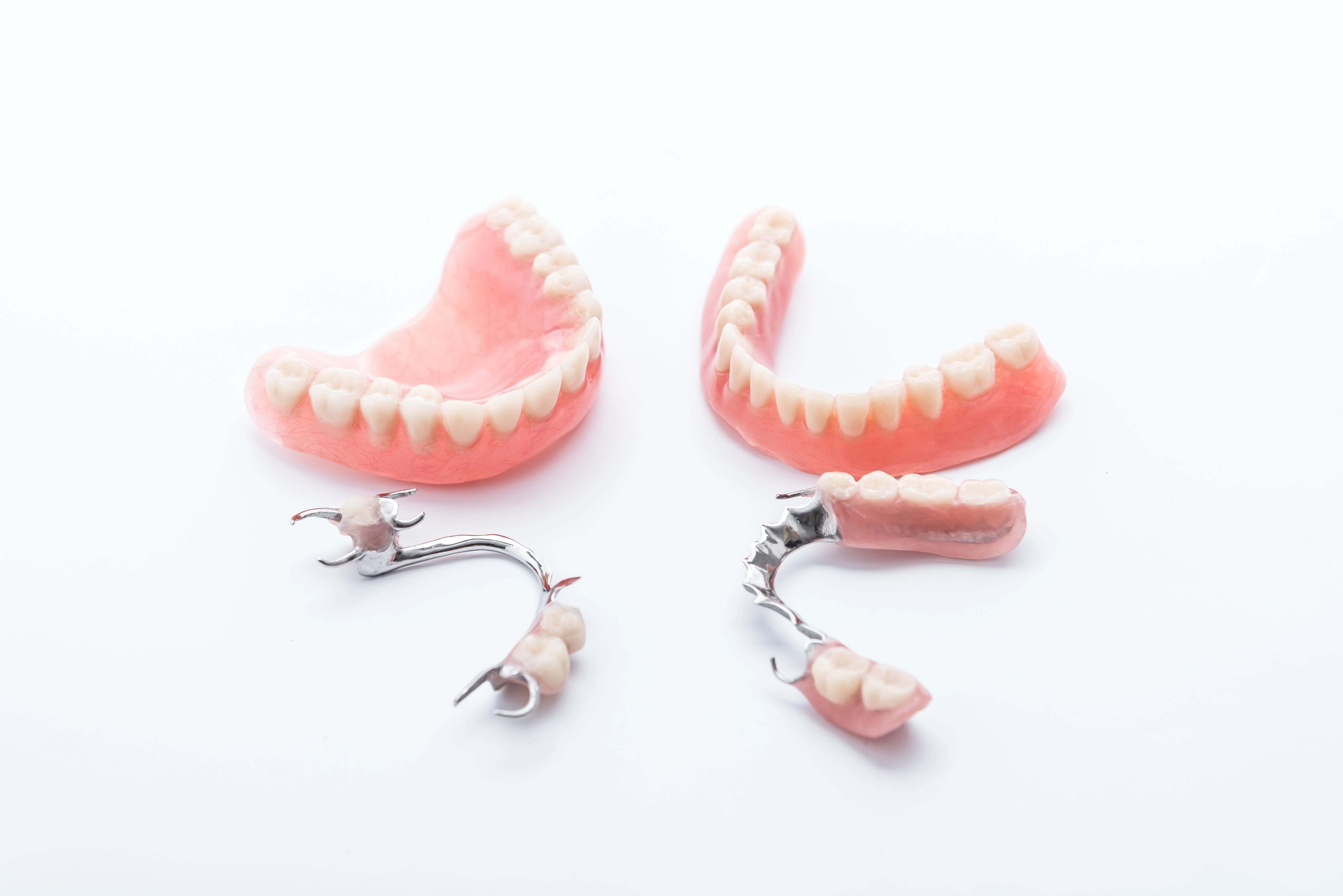 A set of full & partial dentures laid out on a white surface, showing both upper & lower dental prosthetics with metal clasps on the partials.